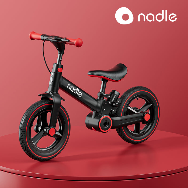 A stylish black and red children's bike displayed on a circular pedestal against a red background.