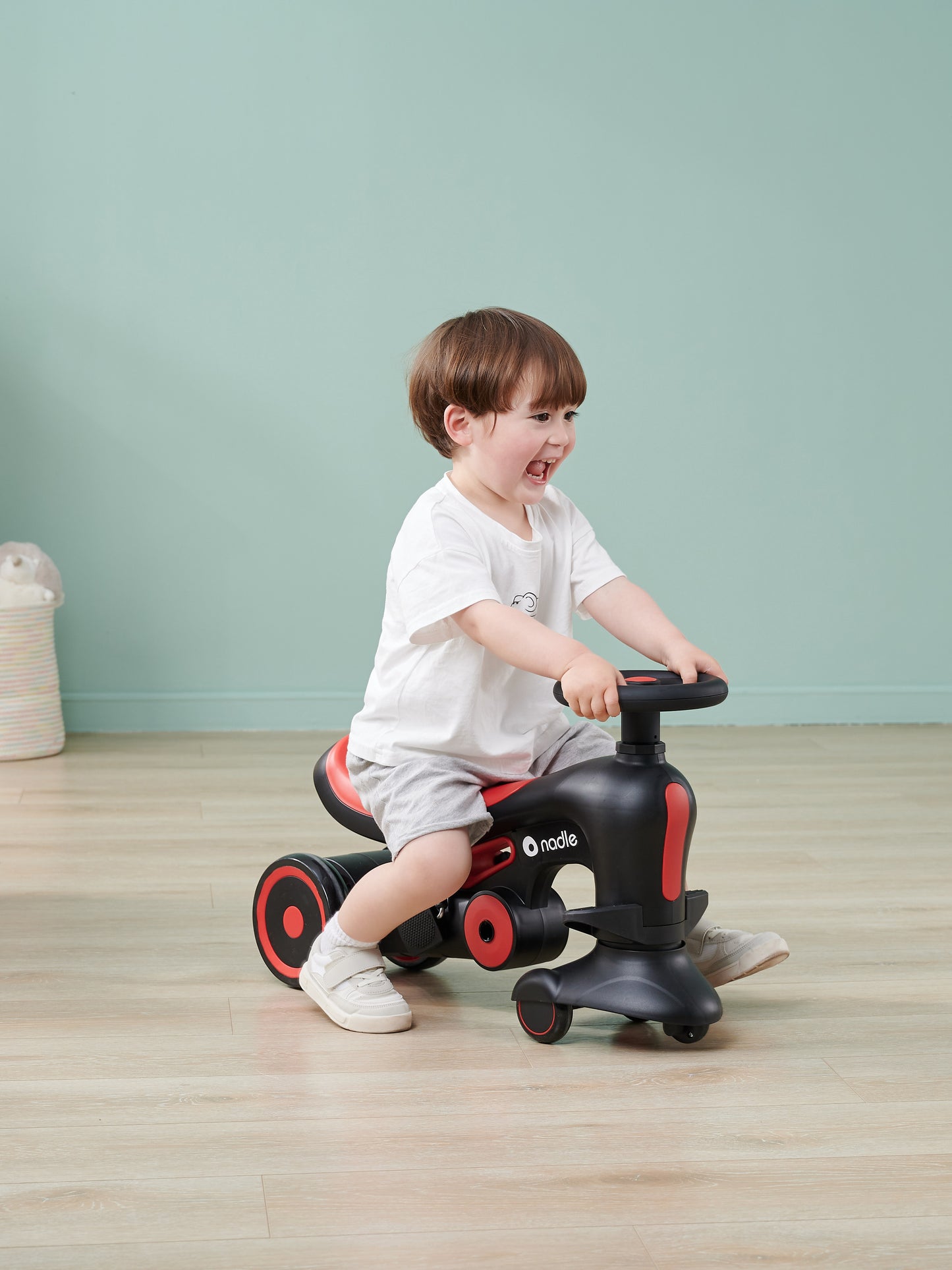 A smiling child riding a black and red toy vehicle, enjoying playtime indoors.